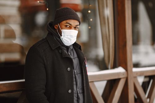 Free Man in black winter coat wearing a face mask in an outdoor setting during the day. Stock Photo
