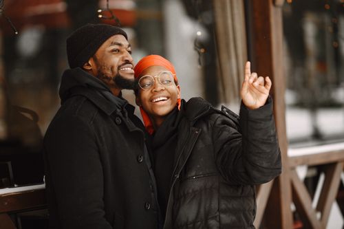 Free Smiling African American couple in warm jackets sharing a joyful moment outdoors in winter. Stock Photo