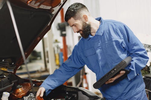 Man in Blue Coveralls Checking on a Vehicle