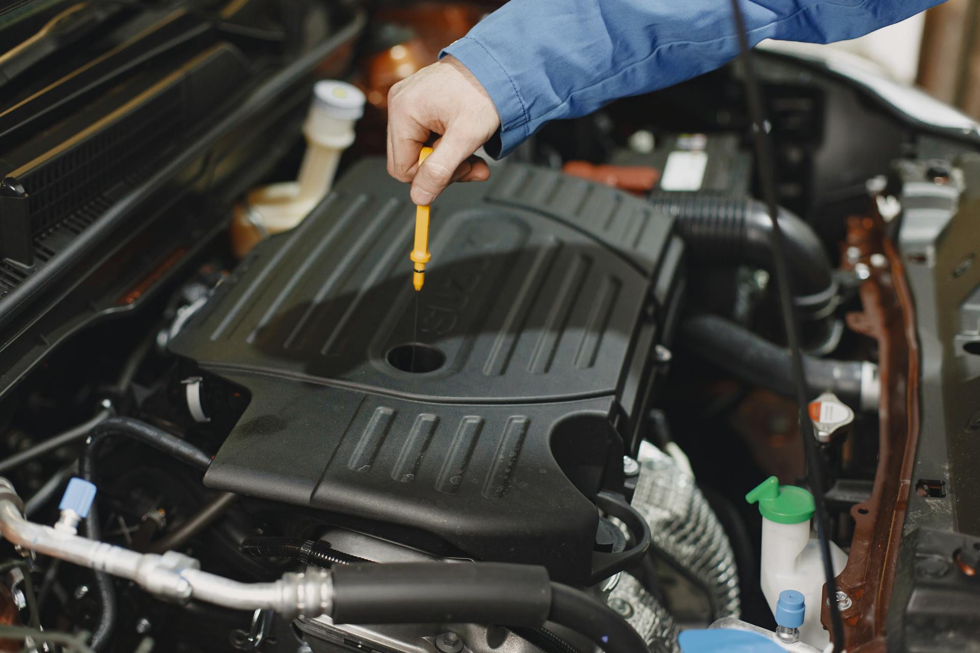 Close-up of a person checking engine oil using a dipstick in a car's engine bay.