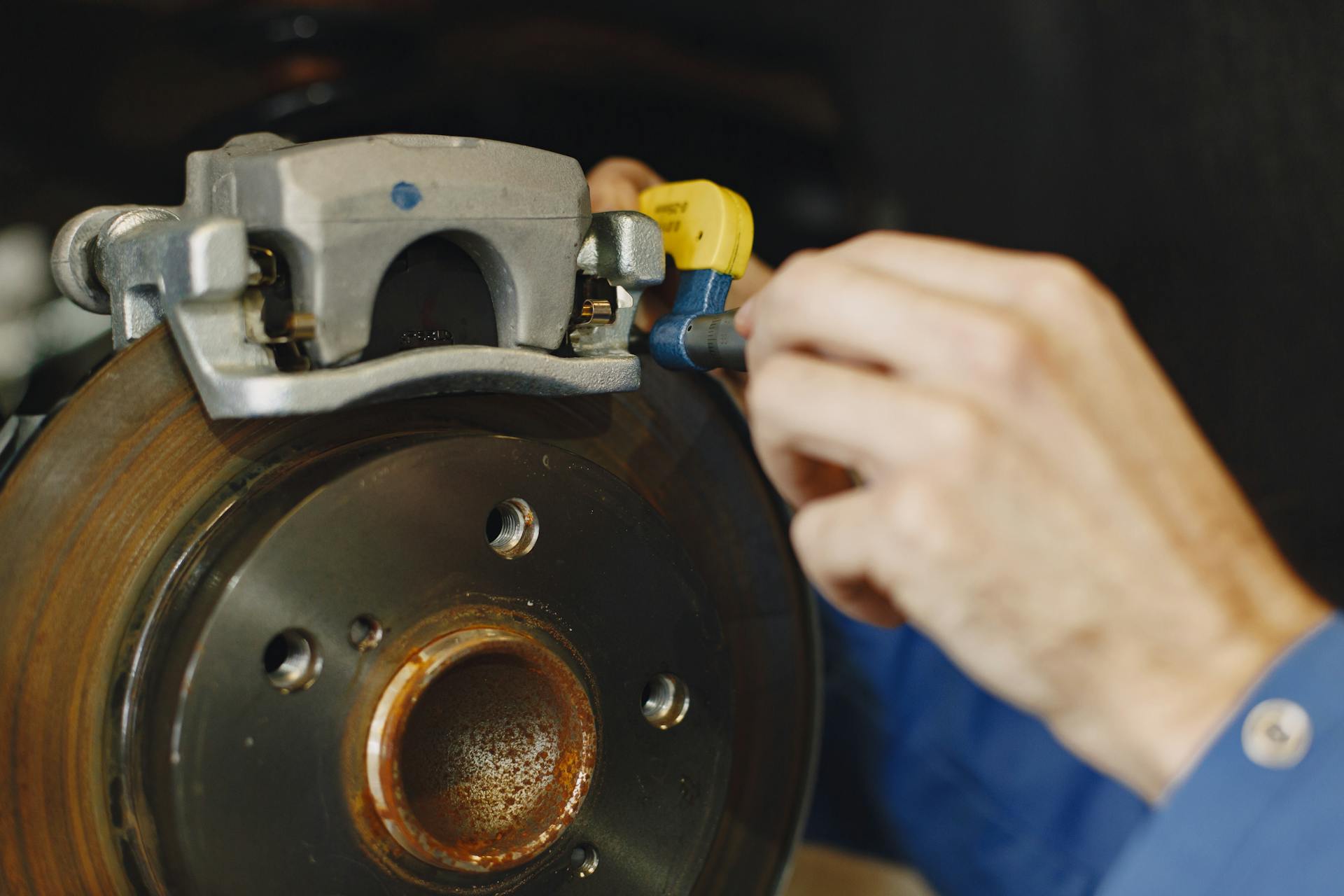 Mechanic working on car disc brake, inspecting for wear and maintenance.