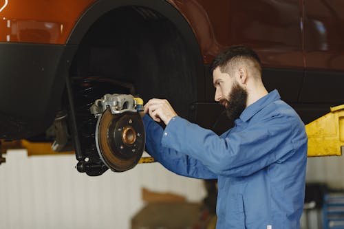 Free Man in Blue Uniform Fixing the Car's Brake System Stock Photo