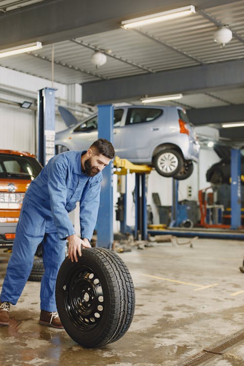 A Man Wearing Blue Uniform Holding a Car Tire