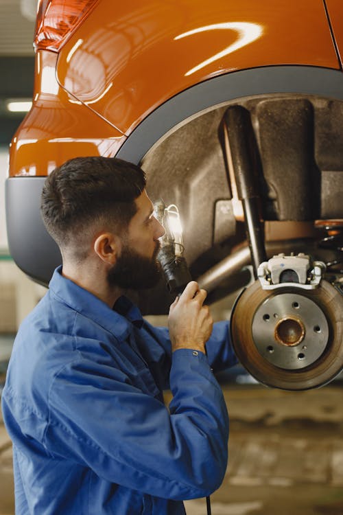 Man in Blue Coveralls Doing Inspection on Brakes of a Car