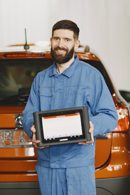 Man in Blue Coveralls Holding an Automotive Diagnostic Tool