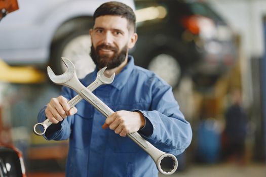 Mechanic in blue uniform holding wrenches inside an auto repair shop, ready for vehicle maintenance.
