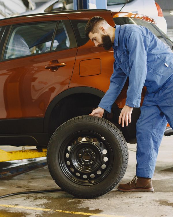 Mechanic in blue coveralls replacing tire on red SUV in repair shop garage.