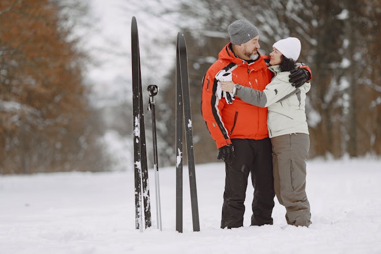 A Couple Standing On Snow Covered Ground With Skis