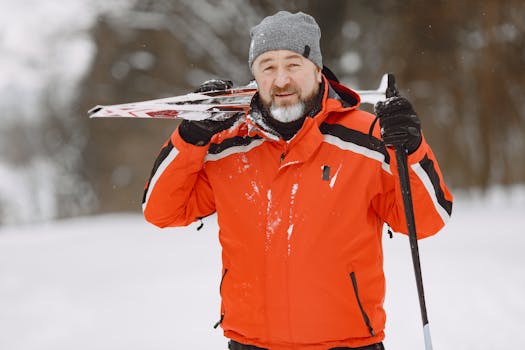 An adult skier in an orange jacket enjoying a snowy winter day outdoors with skis.