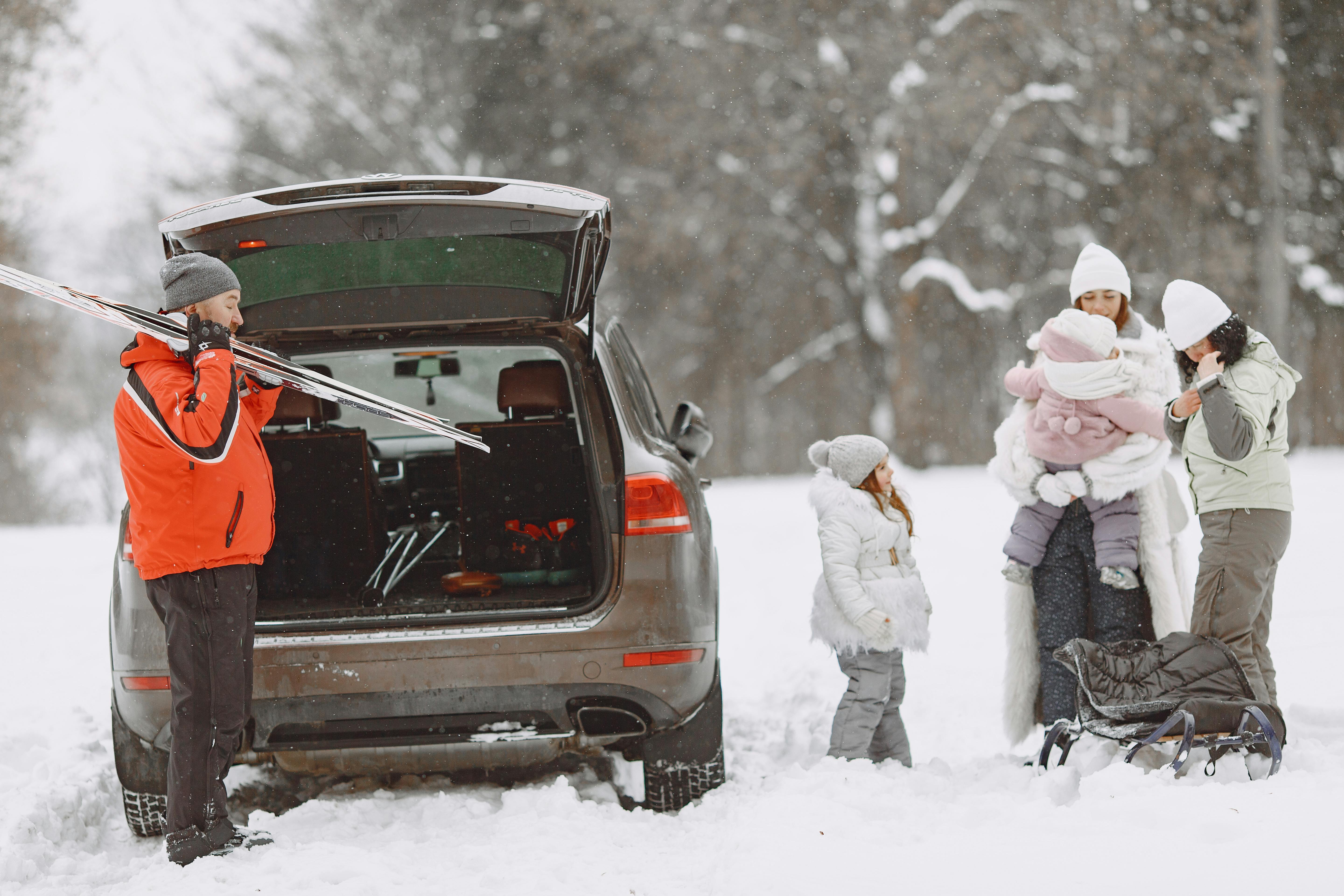 A family gears up for winter fun, unpacking skis and sleds from a car in a snowy landscape.