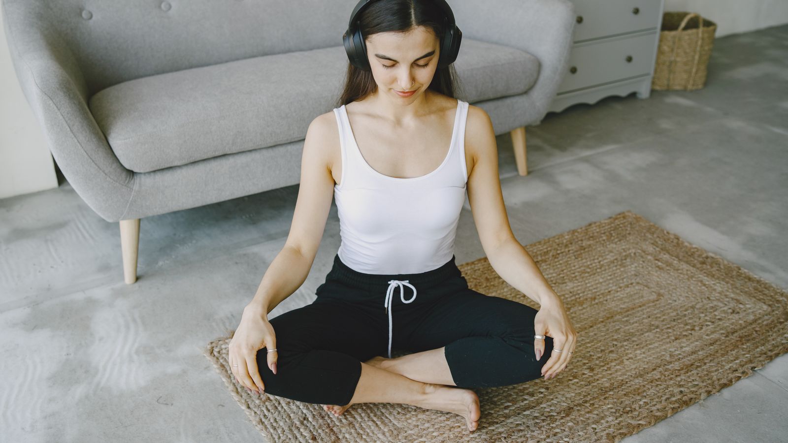 A woman meditating cross-legged indoors while wearing over-ear headphones