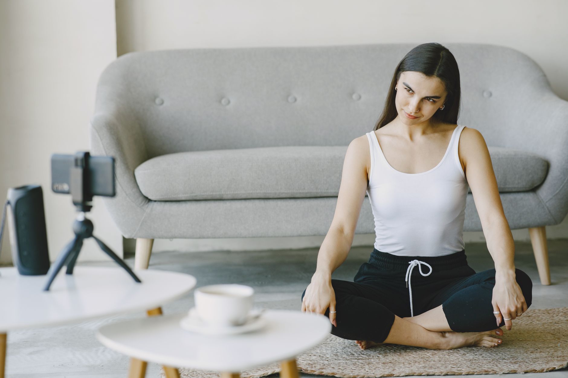 A woman in workout attire doing yoga at home, recording on a smartphone.