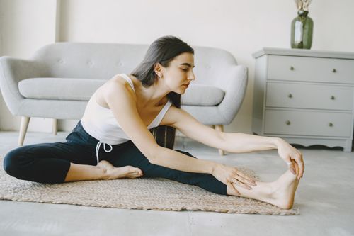 Free A woman in a tank top stretching indoors, promoting relaxation and wellness. Stock Photo