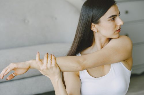 Free A young woman in a white tank top stretching indoors, focusing on fitness and well-being. Stock Photo