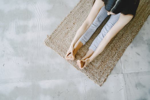 Top view of a woman practicing seated forward bend on a woven mat indoors.