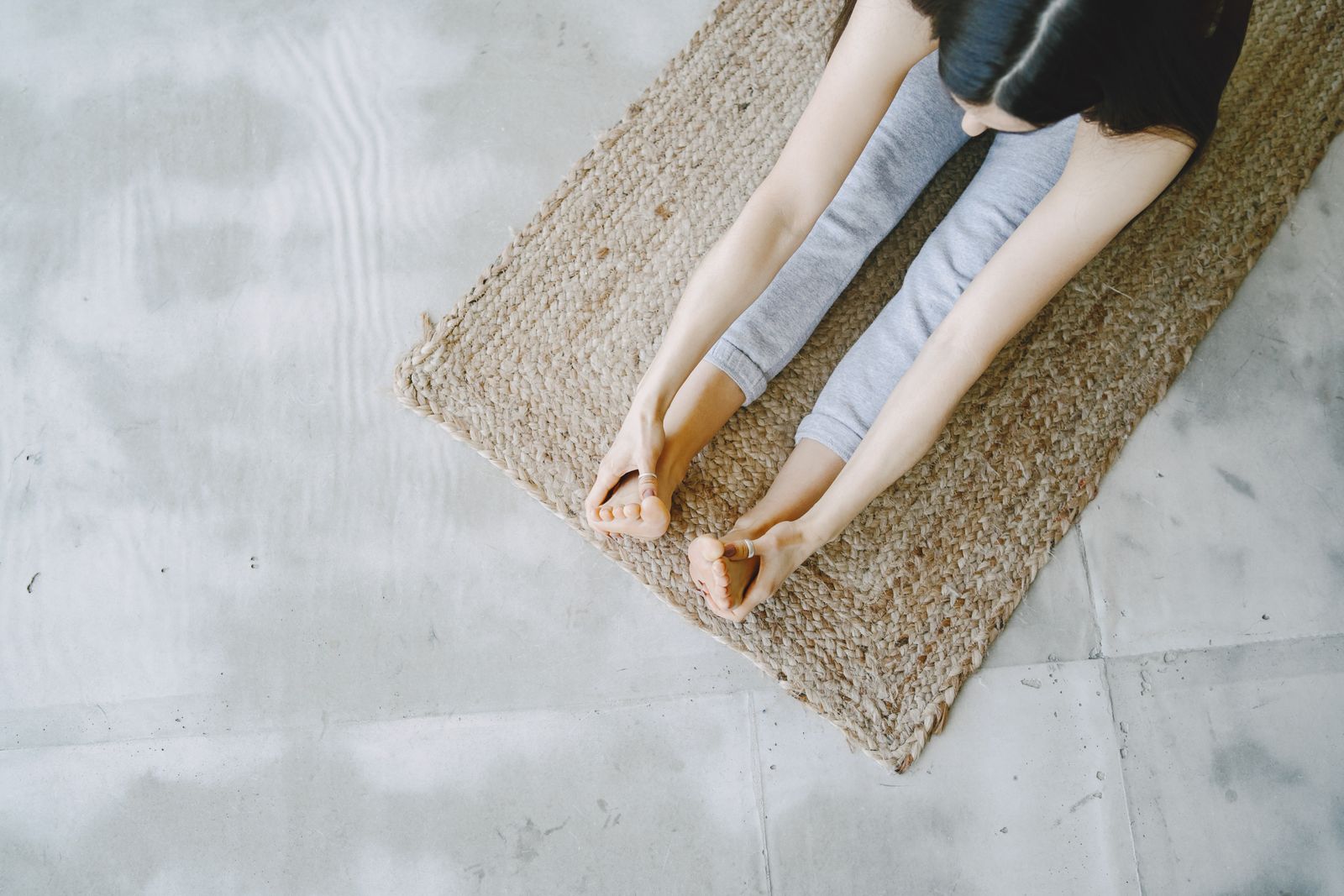 Woman practicing seated forward bend yoga pose on a woven mat for stress and migraine relief
