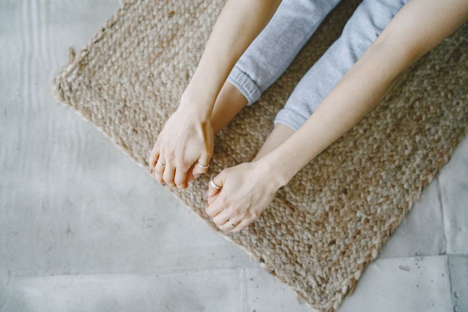 A person stretching on a woven mat. Close-up view of hands and feet in relaxed yoga pose.