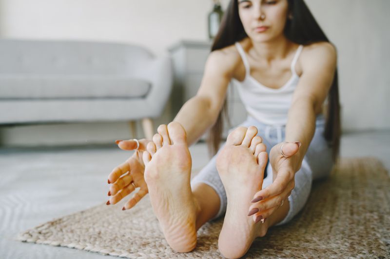 Young woman stretching on yoga mat indoors to relieve morning stiffness
