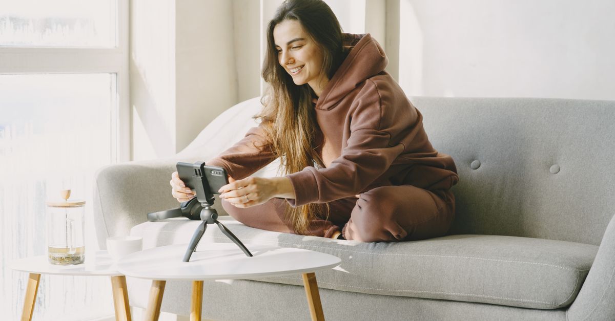 A woman in a cozy setting vlogs using her smartphone on a tripod at home.
