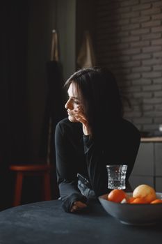Caucasian woman in dark outfit gazing outside, in a pensive mood with hand on cheek.