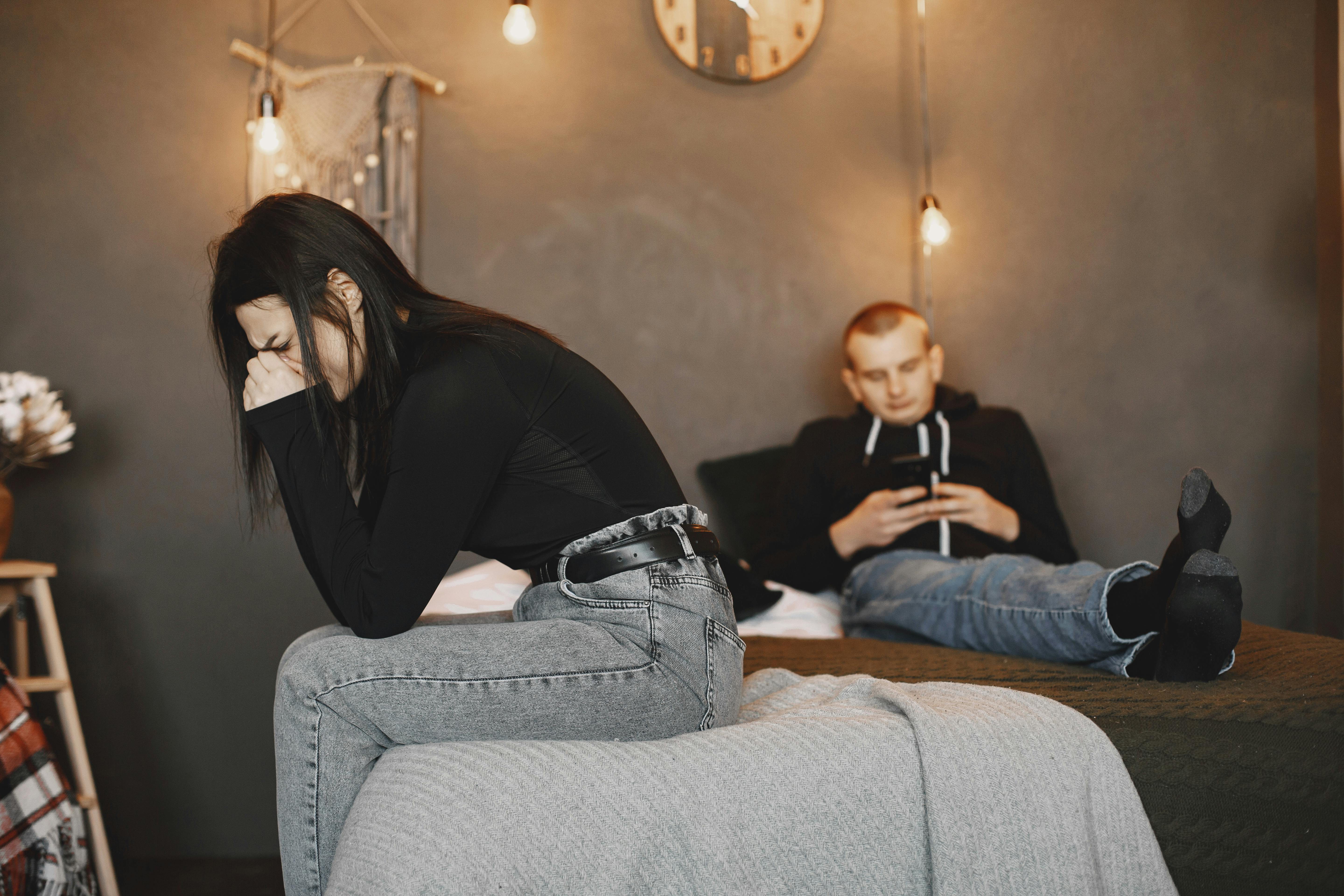 Partnerinden gizlice telefonuna bakan ve mesajlaşan bir kişi, arka planda ise endişeli ve şüpheci bir şekilde onu izleyen sevgilisi.