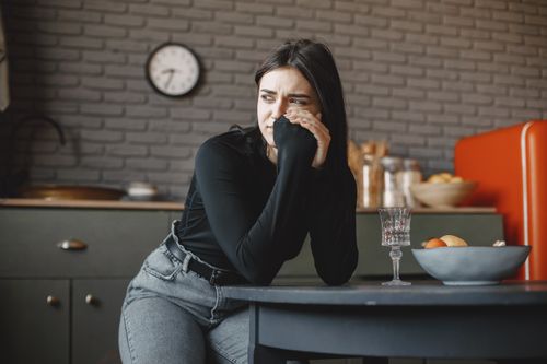 Free Young woman in a pensive mood, sitting indoors with a clock in the background. Stock Photo
