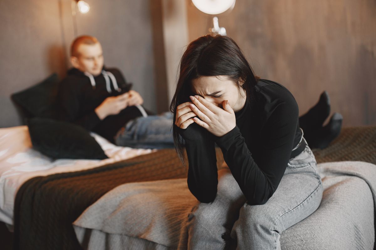Vrouw die huilt op de rand van het bed terwijl haar partner wegkijkt