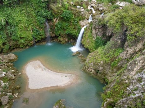 Aerial view of a serene waterfall cascading into a turquoise lagoon surrounded by greenery.