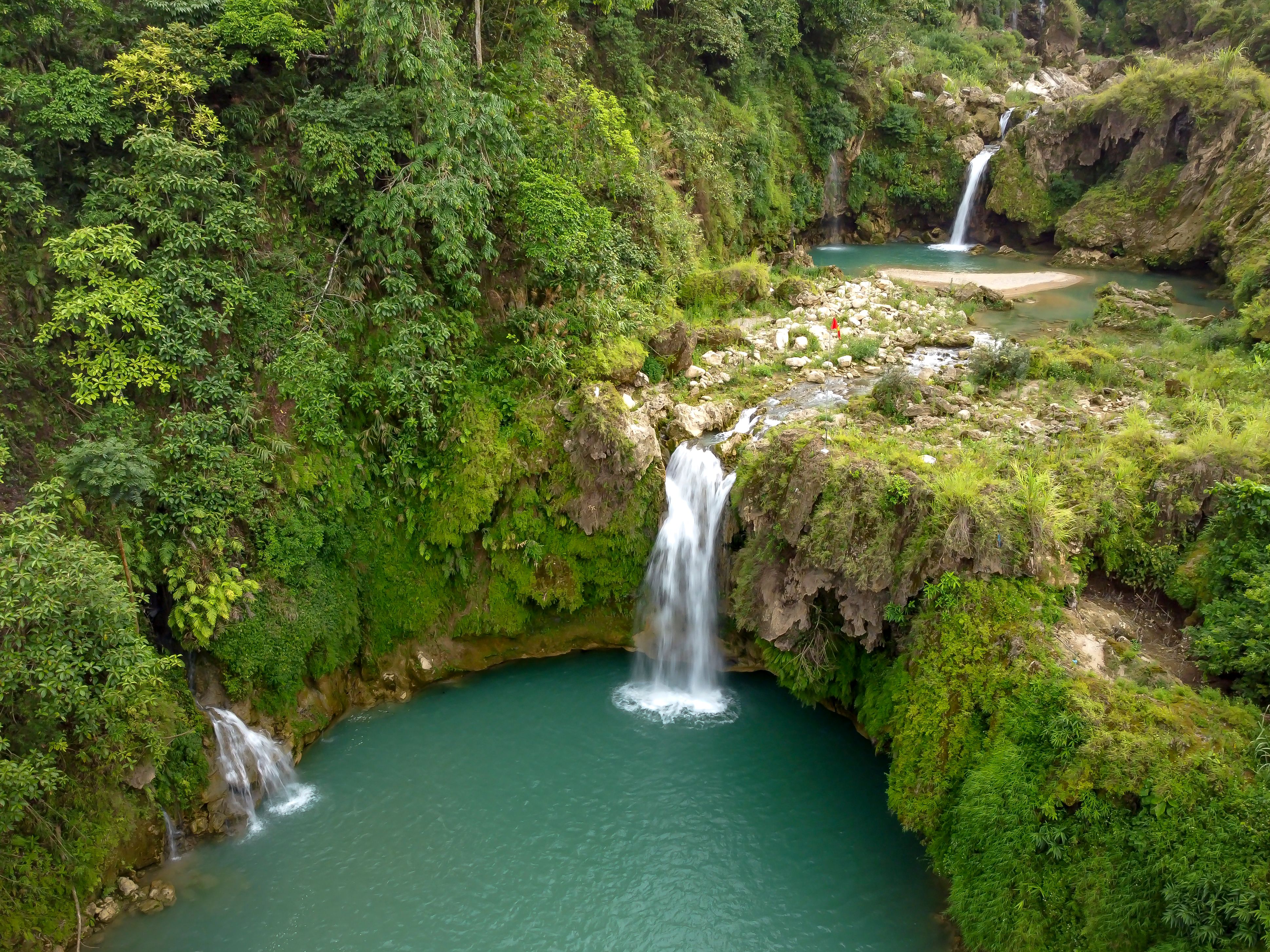 Discover breathtaking waterfalls amidst lush greenery in this vibrant aerial shot.