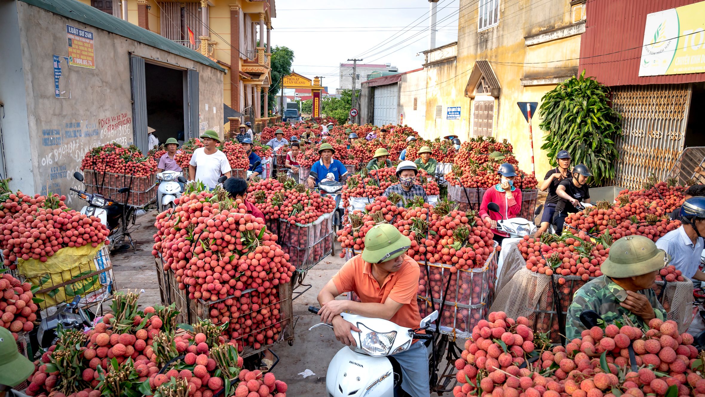 A bustling street market in Vietnam with vendors on scooters selling fresh lychees.