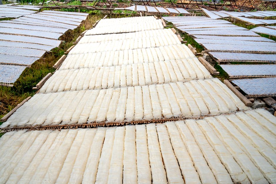 Dark green-black dried kombu sheets stacked with a white mineral bloom visible on the surface, next to a pot of water for making dashi.