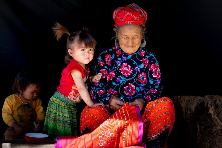 Grandmother And Child In Traditional Clothes Sewing