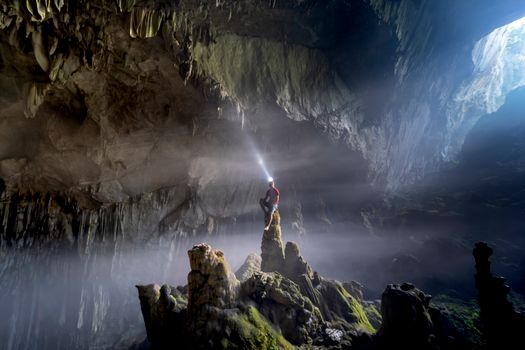 Adventurer with a headlamp illuminating a vast, rocky cave interior.