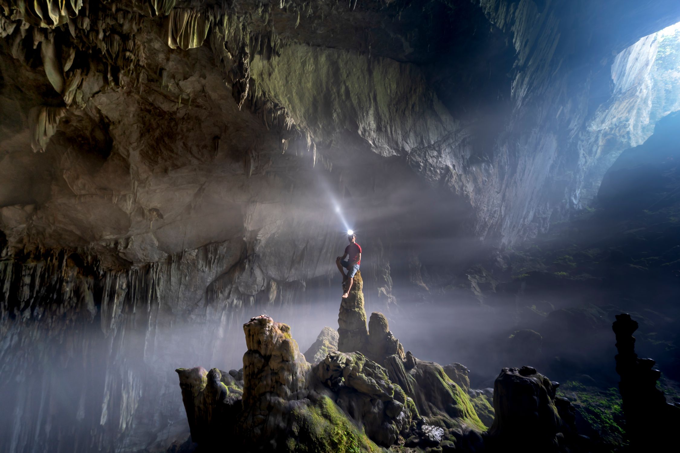 Adventurer with a headlamp illuminating a vast, rocky cave interior.