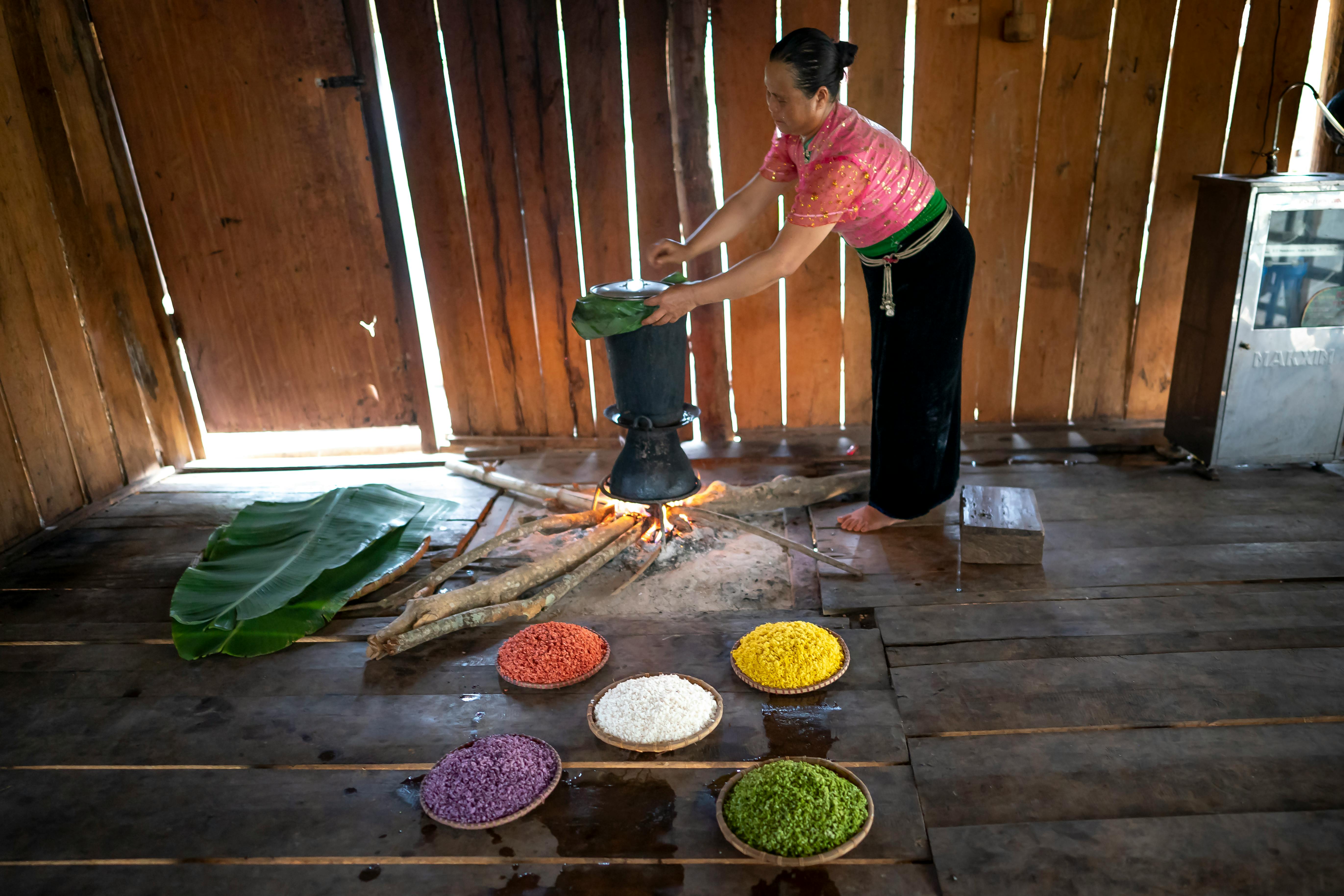 Woman preparing food using banana leaves and firewood in a traditional cooking setup.