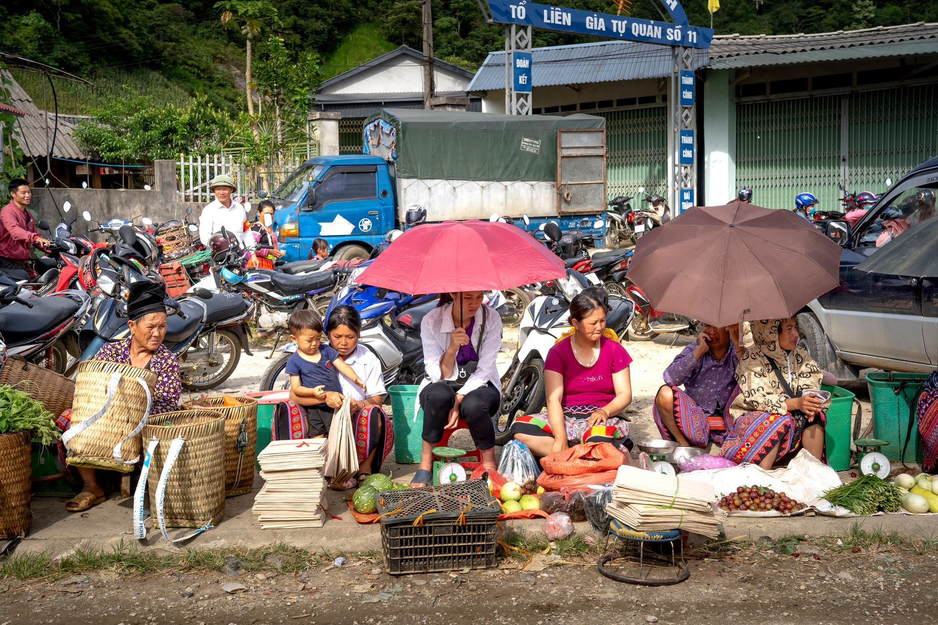 A vibrant rural market with local vendors selling fresh produce and goods under umbrellas.