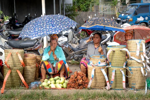Women market vendors sell woven baskets and produce under umbrellas on a busy street.
