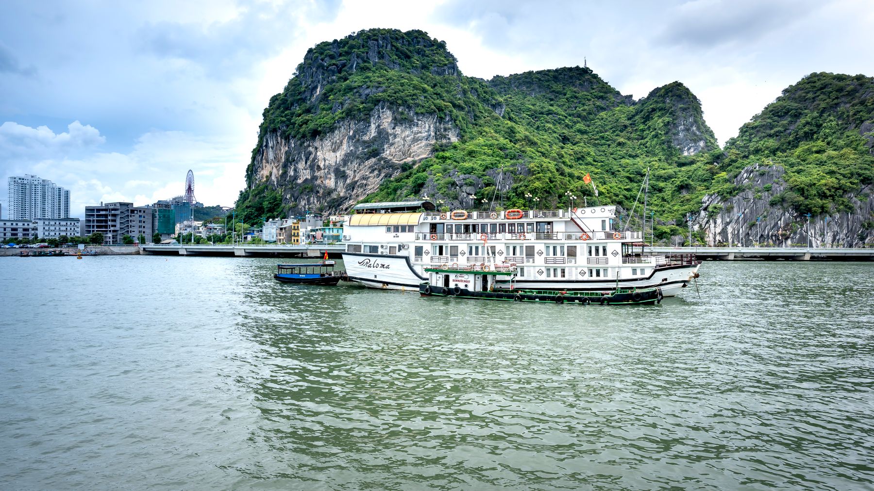 Idyllic boats in Halong Bay with limestone cliffs and cityscape backdrop.
