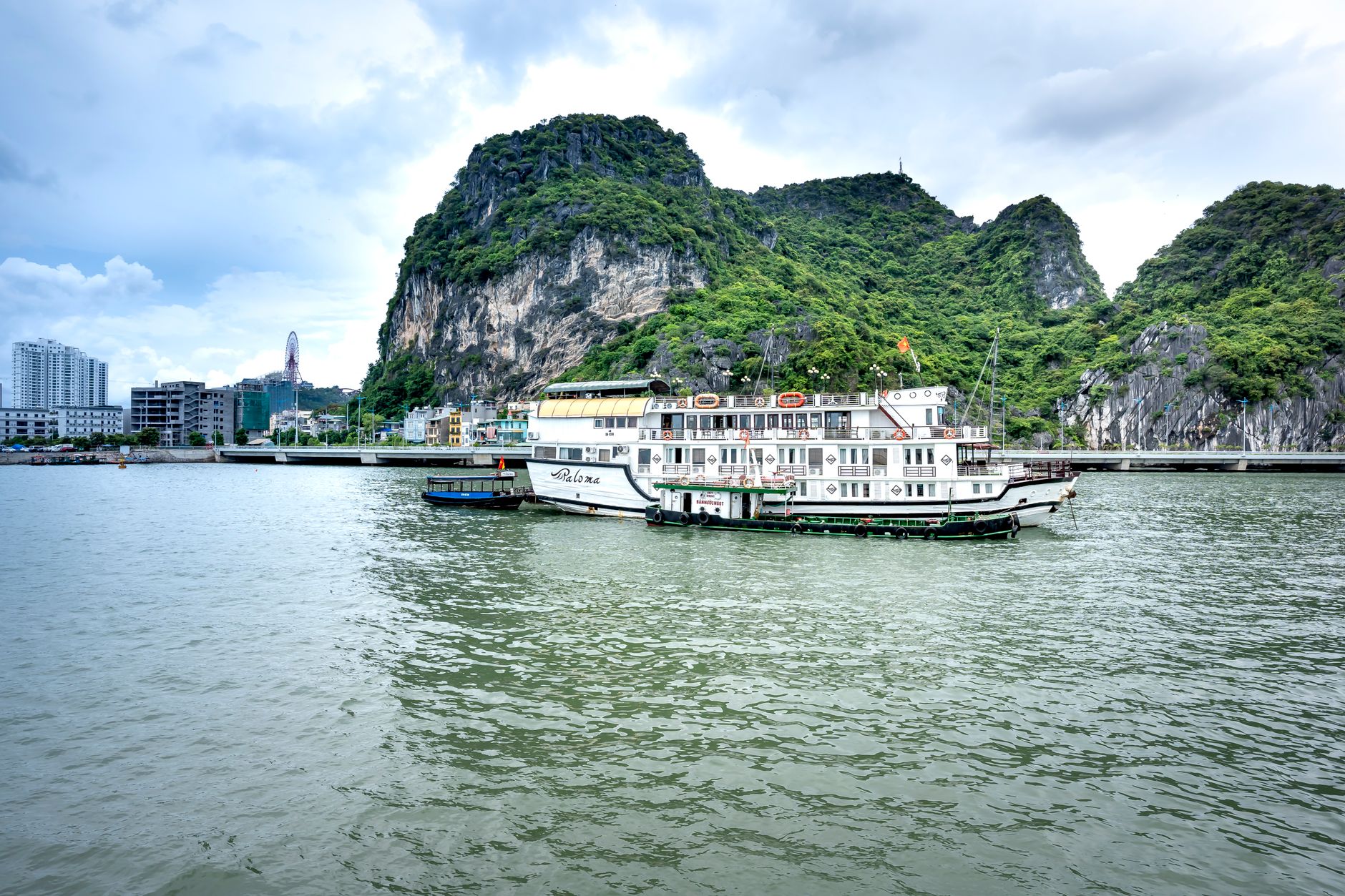 Idyllic boats in Halong Bay with limestone cliffs and cityscape backdrop.