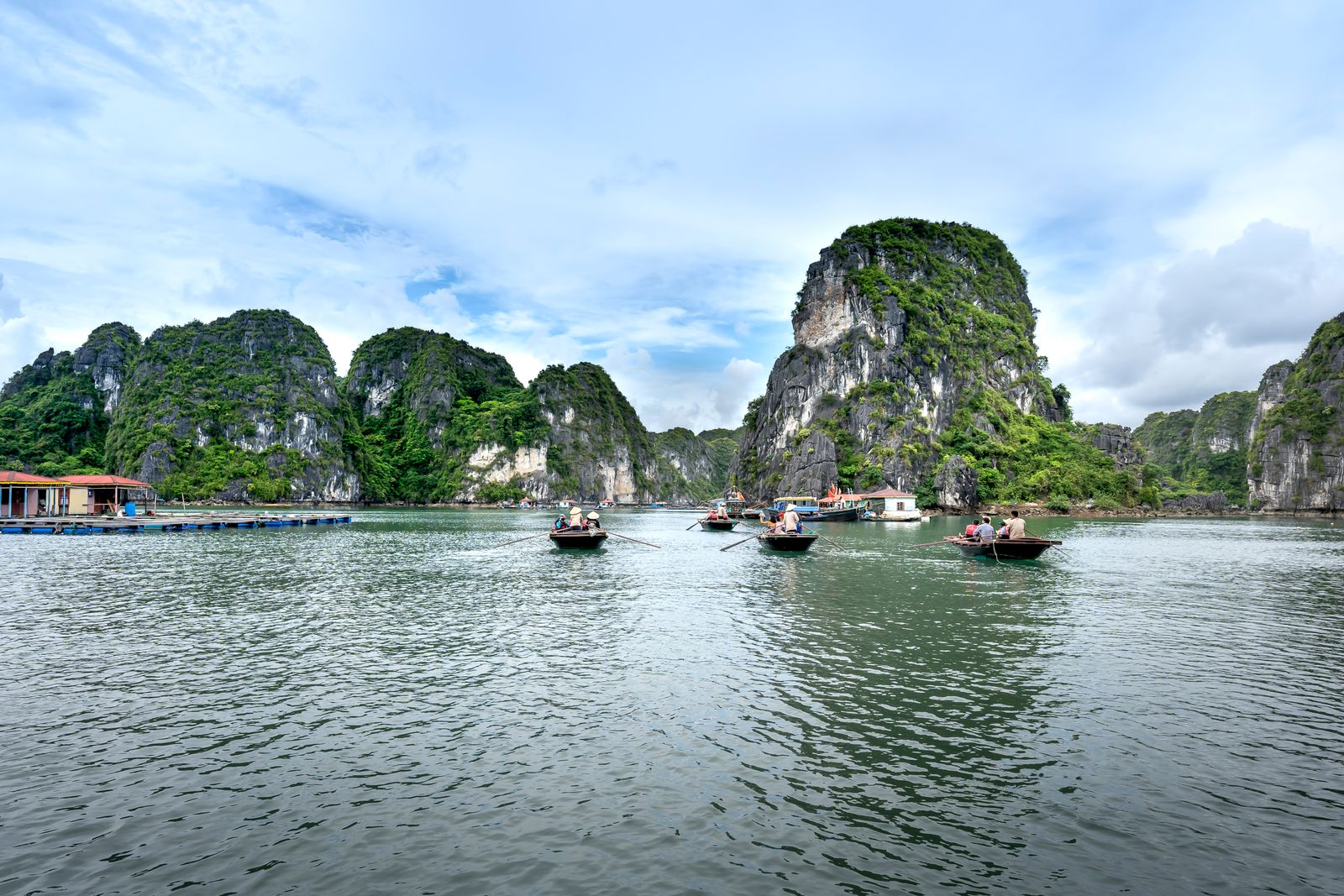 Small boats among tall green limestone karsts on calm water in Ha Long Bay, Vietnam