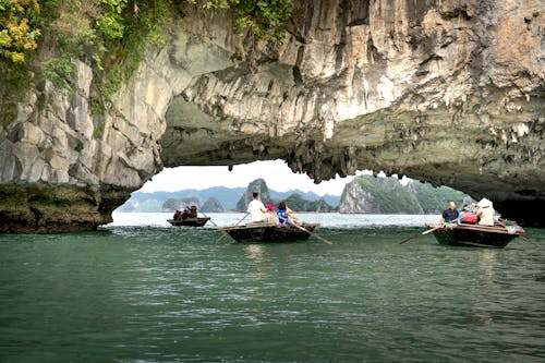 People in Boats Sailing under Rock