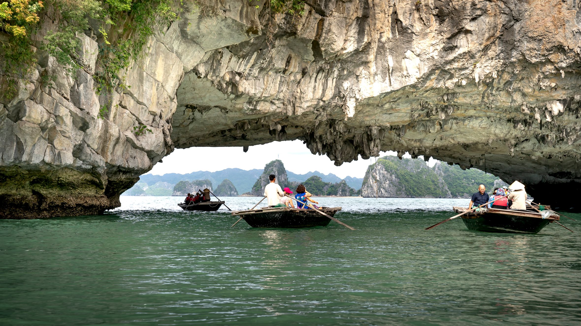 Explore a breathtaking limestone arch with boats on a serene waterway, surrounded by nature.