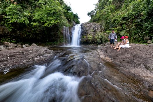 A family sits near a beautiful waterfall in a lush forest landscape, perfect for nature retreats.
