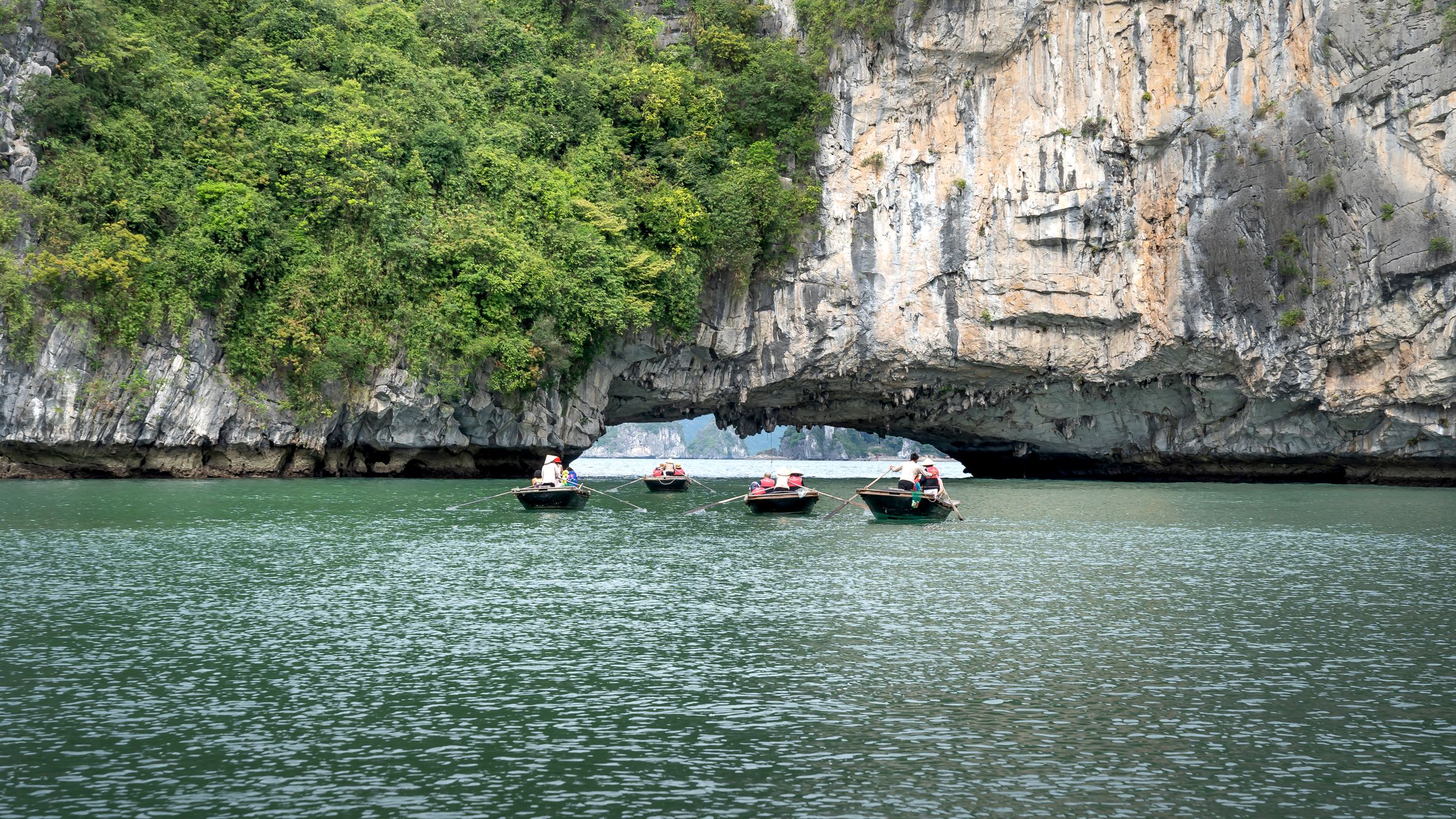 Boats journey through lush limestone cliffs on serene emerald waters, exploring nature's beauty.