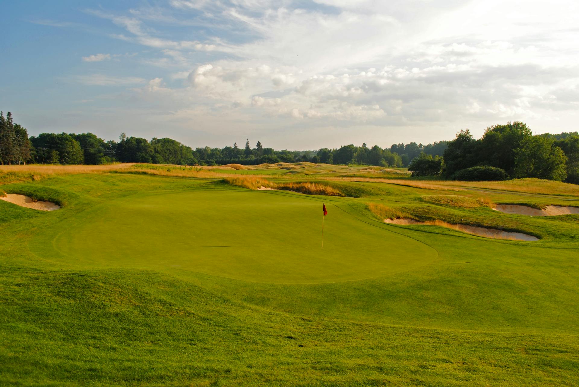 Picturesque scenery of green grassy golf course with holes surrounded by lush forest in hilly terrain on sunny day