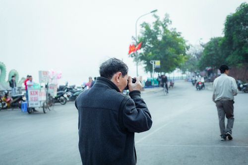 Free Senior adult capturing lively street with camera, flags, and passersby in vibrant setting. Stock Photo