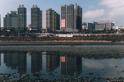Serene cityscape with buildings reflecting in a calm river under a clear sky.