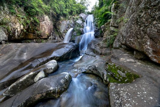 A tranquil waterfall flows over rocks in a lush forest setting, perfect for nature themes.