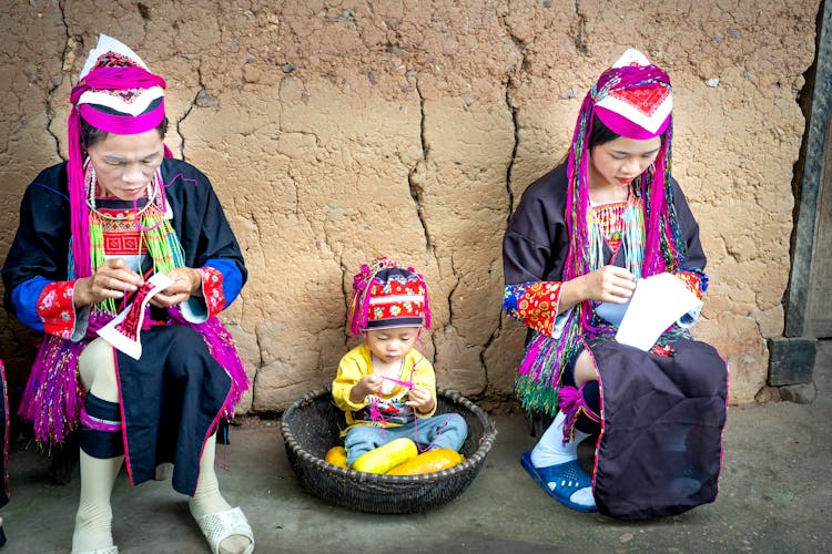 Family In Traditional Clothes Sewing Outdoors