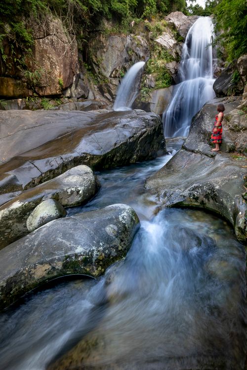 Free A peaceful waterfall cascades over rocks as a person stands nearby, enjoying the scenery. Stock Photo